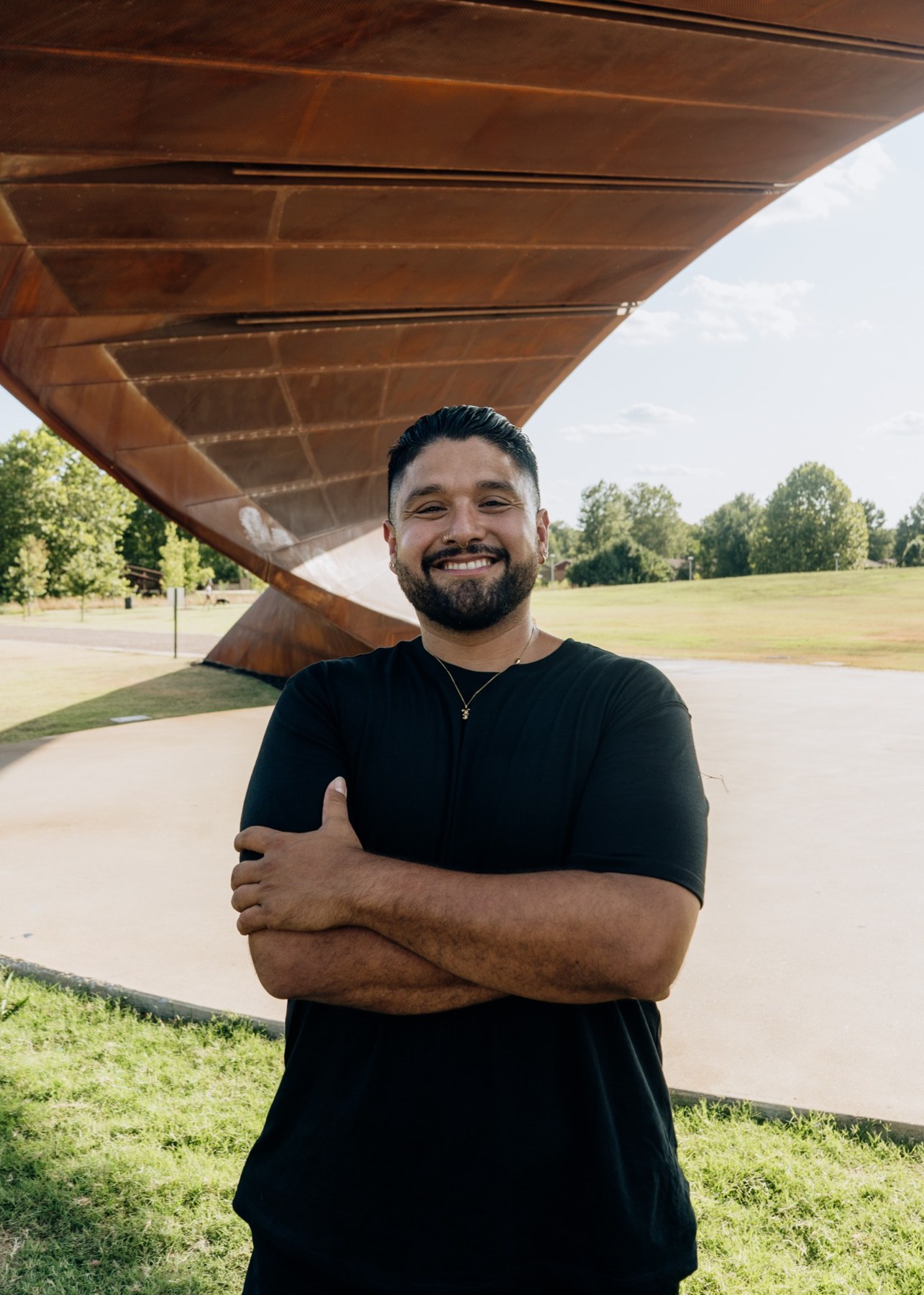 Armando Garcia smiling with his arms folded beneath a pavilion in the park